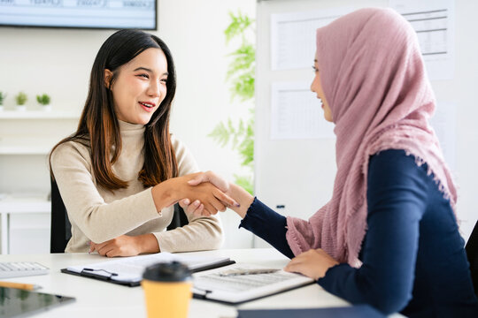 Multiracial young female employees handshake greeting or get acquainted brainstorming working together at laptop, smiling multicultural woman leaders shake hands closing deal at meeting, cooperation.