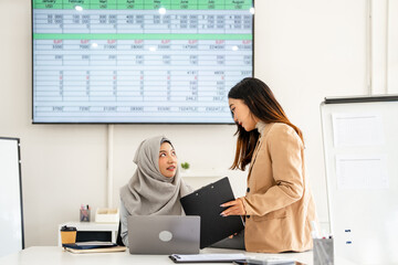 Teamwork process. Asian Muslim businesswoman and coworker  sitting at desk working together in a...