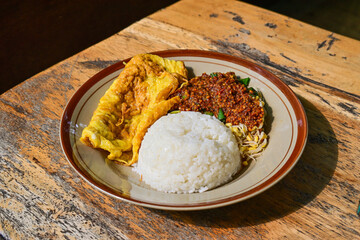 Nasi pecel or sega pecel is a typical Javanese Indonesian rice dish served with pecel. spicy hot peanuts sauce, vegetables and fried chicken egg. Top view. Wooden table. Close up. High angle. Above.