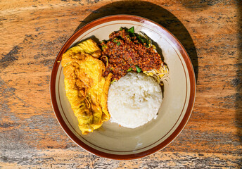 Nasi pecel or sega pecel is a typical Javanese Indonesian rice dish served with pecel. spicy hot peanuts sauce, vegetables and fried chicken egg. Top view. Wooden table. Close up. High angle. Above.