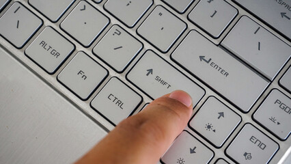 Full frame and close up view of finger pressing shift button of a laptop keyboard isolated on black...