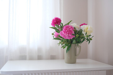 A beautifully charming arrangement of pink and white peonies in a simple vase on white vase.