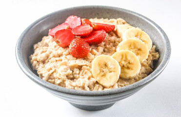a bowl of oatmeal porridge with strawberries and bananas on top, isolated on a white background