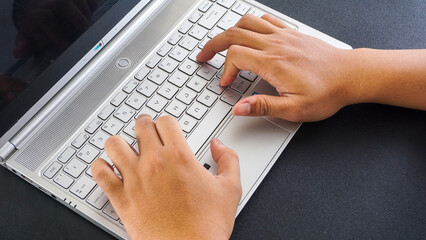 Hands of a man typing on laptop keyboard isolated on black background