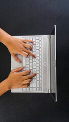 Top view of hands of a man typing on laptop keyboard isolated on black background
