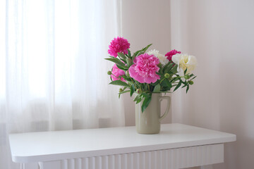 A beautifully charming arrangement of pink and white peonies in a simple vase on white vase.