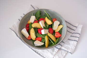 A vibrant salad of fresh ingredients - peaches,spinach, strawberry, cheese drizzled with olive oil, showcasing the essence of healthy eating.