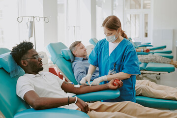 Young Black man donating blood while female healthcare worker preparing needle, middle aged...