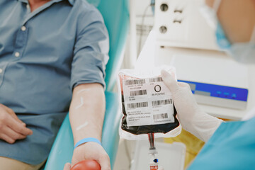 Caucasian middle aged man donating blood while medical worker holding blood bag labeled O positive,...
