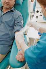 Middle aged Caucasian man sitting in medical chair receiving care from female healthcare worker...