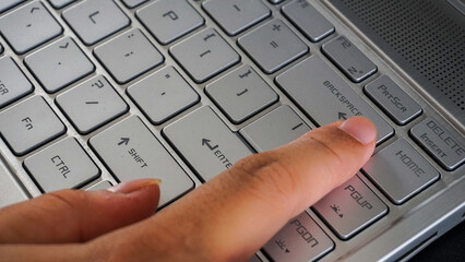 Finger pressing backspace button of a laptop keyboard isolated on black background