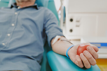 Middle aged Caucasian man donating blood in medical facility, lying on chair with blood collection...