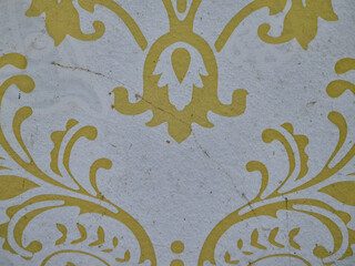 Close-up of vintage yellow floral pattern on textured white wallpaper with visible stains