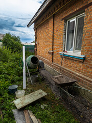 Construction work with concrete around a brick house, concrete mixer and wheelbarrow