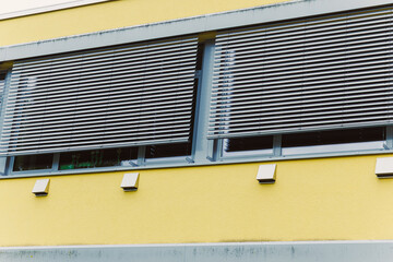 The innovative and modern design of architectural windows incorporates elegant blinds and showcases a vibrant yellow facade, creating a striking appearance that enhances urban aesthetics
