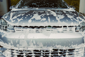 A sparkling clean car, covered in soapy foam, sits at a busy car wash, gleaming in the sunlight....