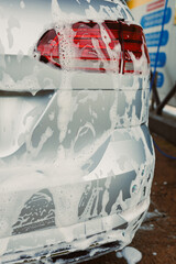 A shiny silver car, thoroughly covered in foam, is undergoing a meticulous cleaning process at an...