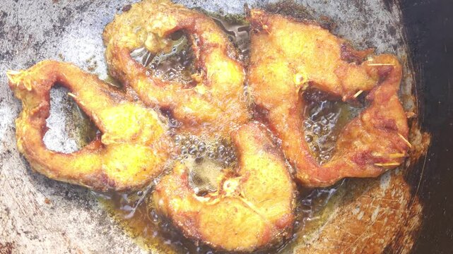 Close-up fish pieces sizzle over the open flame in a frying pan, their golden crust forming in a close-up dance of flavors&mdash;an ode to the traditional style of spicy fish fry. 8k footage