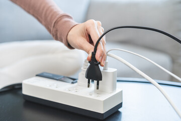 Closed up hand of woman plugged in, unplugged electricity cord cable on socket on table for energy...