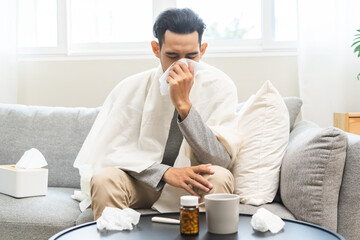 Sick, influenza asian young man have fever, hand blowing nose, sneezing in tissue at home while ill...