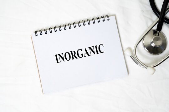 The medical concept "INORGANIC" is written clearly on a white spiral notebook, accompanied by a stethoscope on a white background.