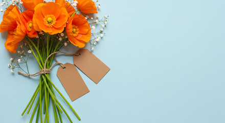 Vibrant orange poppies and baby's breath bouquet, tied with twine and blank tags, on pale blue.
