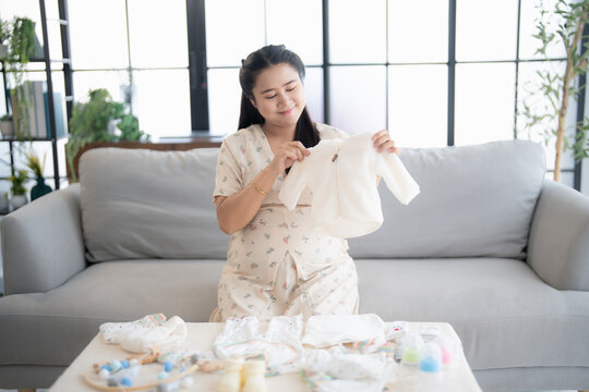 Pregnant asian woman getting ready for the maternity hospital preparing and planning baby clothes for new baby of pregnancy packing baby stuff on bed. - Powered by Adobe