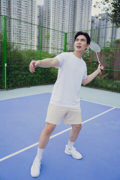 Young man plays badminton outdoors in an urban setting with tall buildings in the background during the day