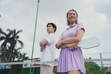 Young Asian athletes pose confidently for a pickleball match in a vibrant outdoor setting