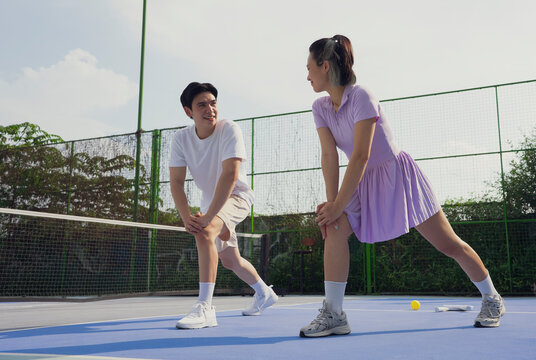 Couple stretching before pickleball match on outdoor court in sunny weather