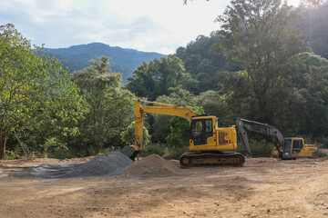 Yellow backhoe with piles of sand and rocks for mixing cement in a forest area for the construction...
