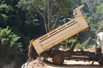 A white truck is dumping sand on the ground on a rural road through a forest being repaired, in the construction area of ​​a road repair contractor.