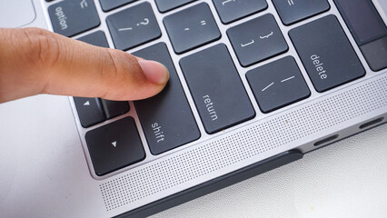 Finger pressing shift button of a laptop keyboard isolated on white background