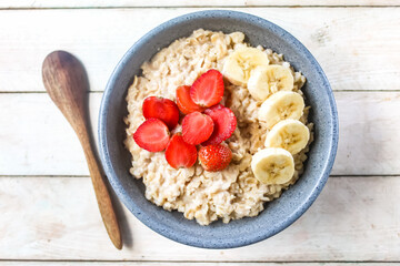 a bowl of oatmeal with strawberries and bananas on top, on a wooden table