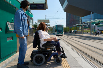 Man assisting woman in wheelchair at modern tram stop - wheelchair and disability concept