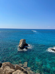 Clear turquoise water surrounds rugged rocks under a bright blue sky. A peaceful seascape ideal for vacation, travel, and nature concepts.