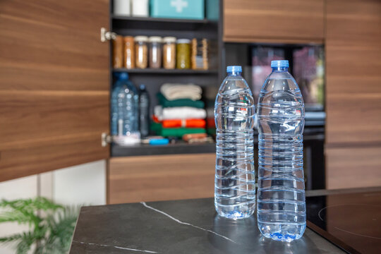 72 hour survival kit with canned food and essential supplies. Water bottles on kitchen counter in front of pantry with emergency food, drink and first aid kit ready for use in war or natural disasters