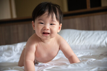 Portrait of adorable naked Asian baby crawling on bed on the white bedsheets in bedroom.