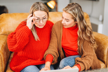Two women sitting on a cozy couch engaged in conversation while looking at a laptop in a modern...