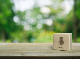 Microphone flat icon on wood block cube on wooden table over blur green tree in park, Business communication concept