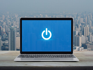 Power button flat icon on modern laptop computer screen on wooden table over city tower and skyscraper, Start up business online concept