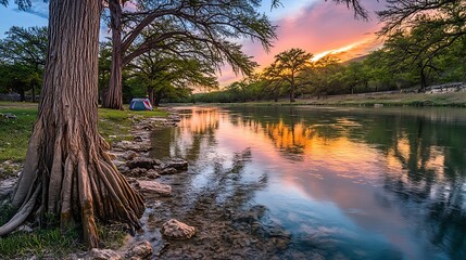 River reflects sunset near trees and a campsite tent