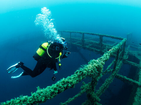 Fototapeta diver diving next to the wreck of a structure submerged in the sea colonized by marine life, concept of scuba diving and underwater adventure