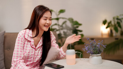 Young Asian Adult Woman Enjoying Aromatherapy Diffuser at Home Promoting Relaxation and Wellness...