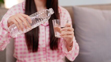 Asian young adult woman demonstrating essential daily hydration habit pouring refreshing water into...
