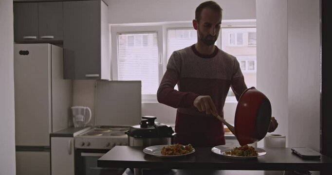 A young man serves a meal of rice and vegetables in a modest kitchen. He prepares and serves the meal with efficiency.