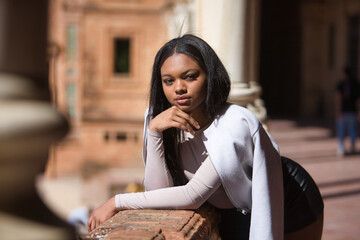 Portrait of young, beautiful, African woman, with leather jacket and shorts, with her hand on her...