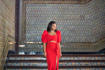 Young, beautiful, African woman, wearing a red dress, posing as a model on the stairs of the square...