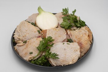 Fresh raw marinated chicken thighs seasoned with spices and parsley in black plate on white table
