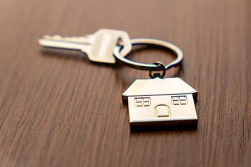 A key attached to a metallic house-shaped keychain on a table. Homeownership, real estate, property...